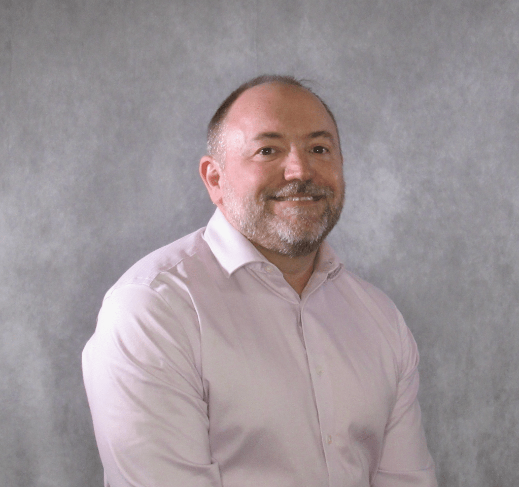 Image of Andrew Molthan standing in a pink shirt in front of a plain studio background.