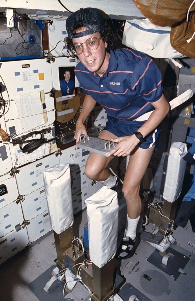 Mission Specialist Ellen Baker exercising on an excercise bike attached to the Isolated/Stabilized Exercise Platform (ISEP) on the shuttle middeck. The ISEP is intended to insulate sensitive microgravity experiments from vibration caused by crew exercise