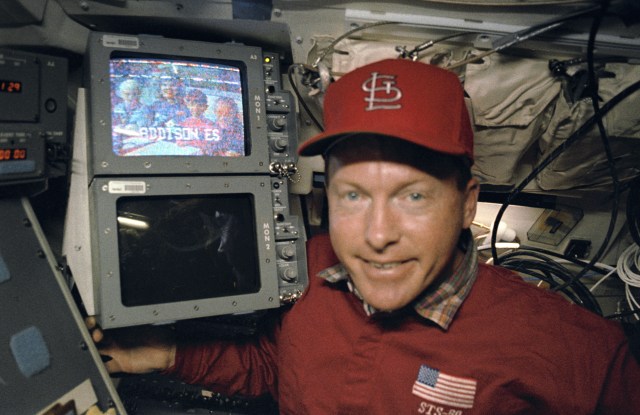 Mission Commander Richard Richards beside the aft flight deck video monitor screen during the simultaneous video and SAREX (Shuttle Amateur Radio EXperiment) broadcast