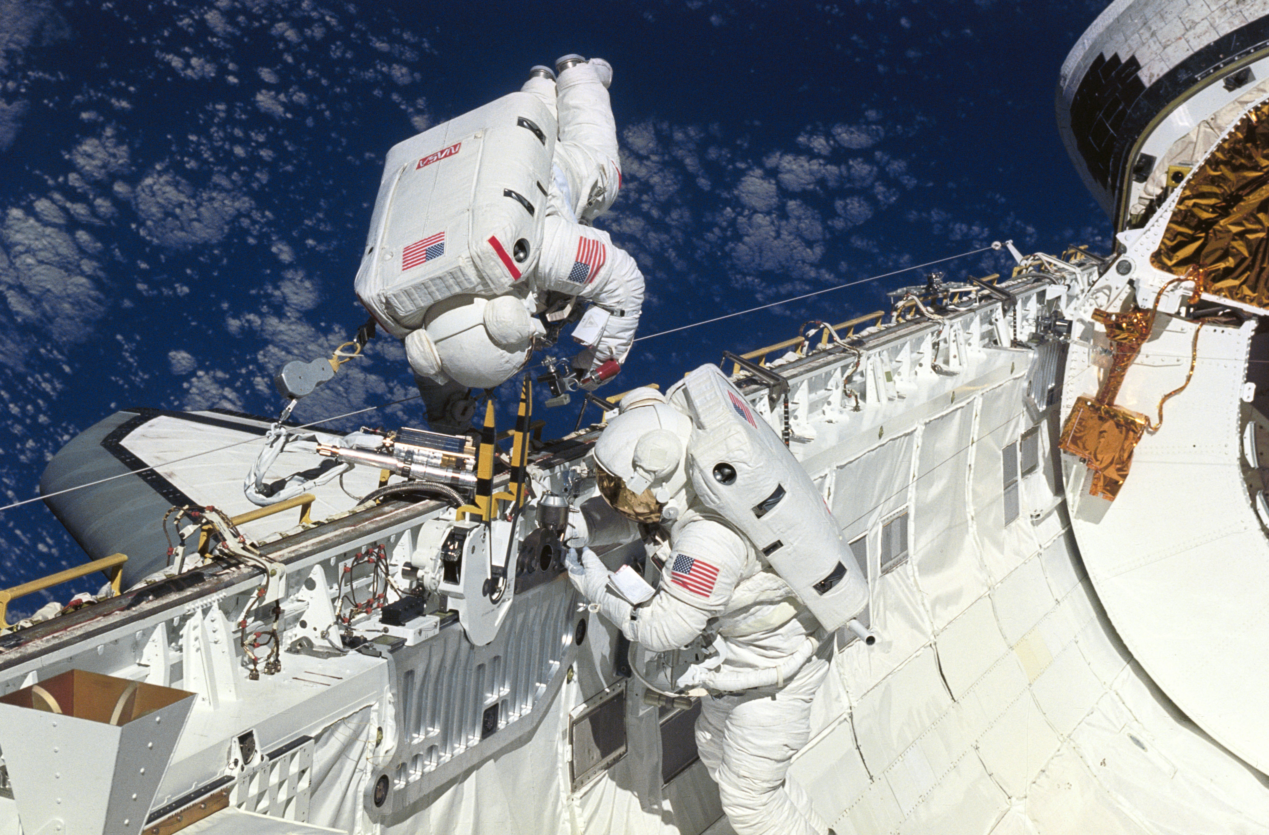 Astronauts James H. Newman (in bay) and Carl E. Walz, mission specialists, practice space walking techniques and evaluate tools to be used on the first Hubble Space Telescope (HST) servicing mission scheduled for later this year. Walz rehearses using the power ratchet tool (PRT). Both men are tethered to the starboard side of the payload bay.