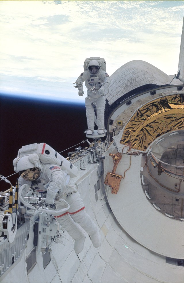 Astronauts Carl E. Walz (foreground) and James H. Newman evaluate some important gear. Walz reaches for the power ratchet tool (PRT) while Newman checks out mobility on the portable foot restraint (PFR) near Discovery's starboard orbital maneuvering system (OMS) pod. The tools and equipment will be used during future extravehicular activities (EVA's).