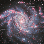 An image of a bright spiral galaxy, which looks like a spiraling swirl of red, pink, white, and pale blue clouds and dots around a white glowing center. Two small white circles highlight supernovae.
