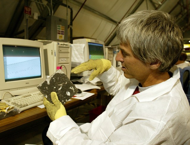 A man in a lab coat and gloves holds one of Columbia's thermal protection system tiles