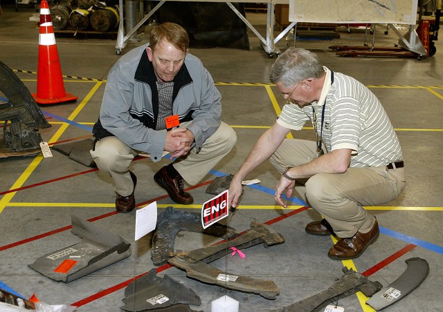 Two men crouch down to look at Columbia debris at KSC
