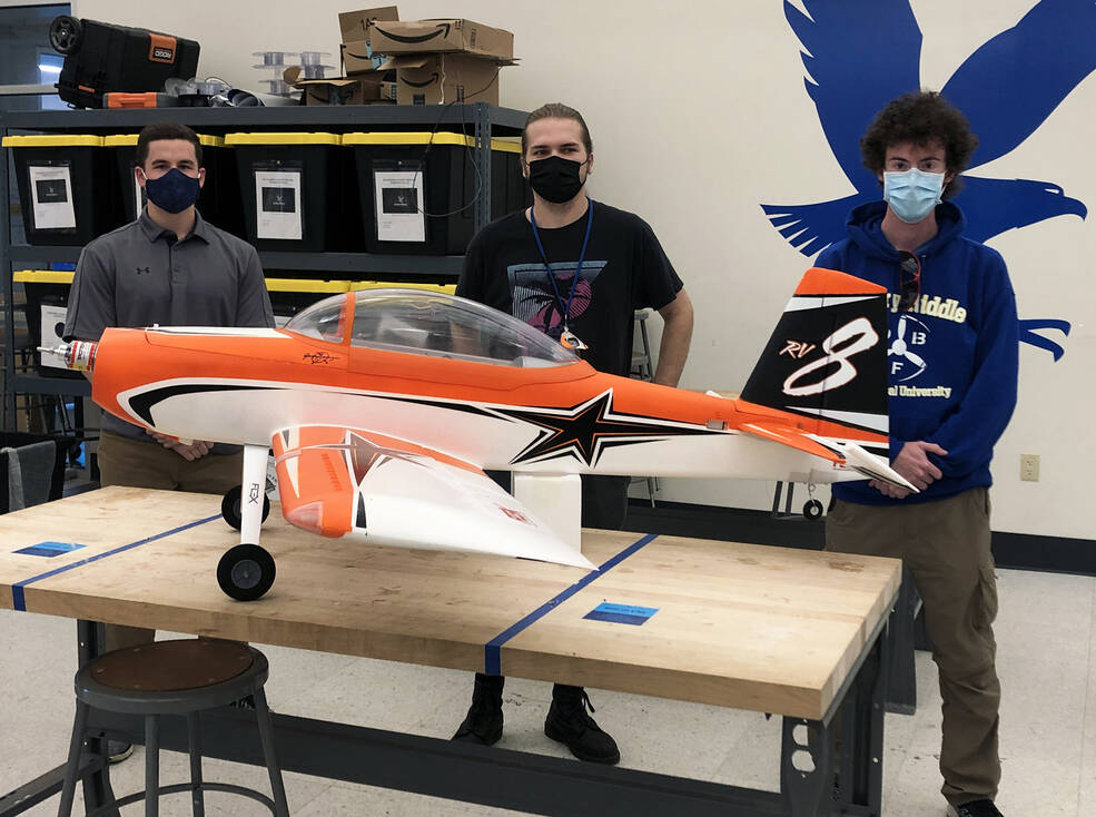University students stand behind a large-scale model aircraft that is sitting on a work bench.