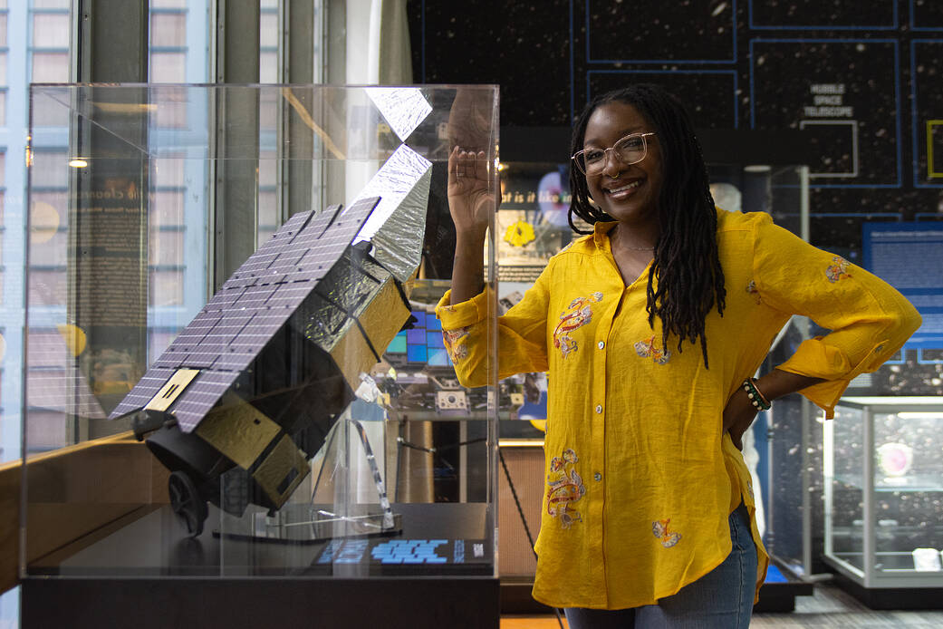 Roman Space Telescope Technical Photographer Jolearra Tshiteya standing next to a display.