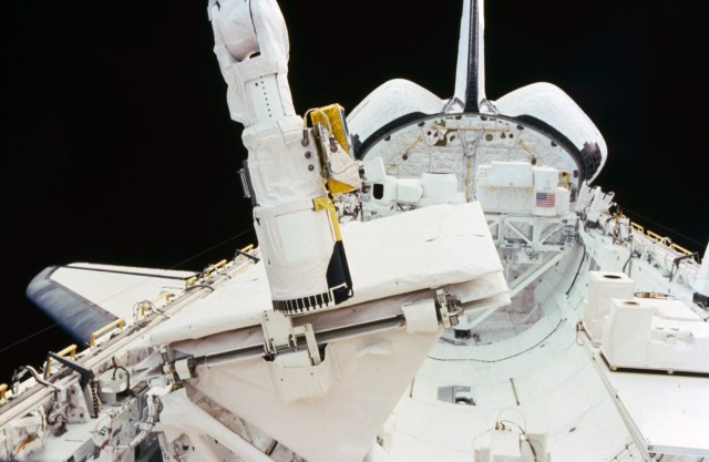 View of the remote manipulator system (RMS) end effector touching the SIR-B antenna to secure it during STS 41-G. The Challenger's payload bay is open and the pallet containing OSTA-3 experiments is visible.
