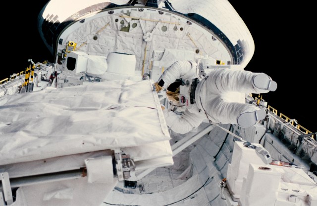Astronaut Kathryn Sullivan checks the latch of the SIR-B antenna in the Challenger's open cargo bay during her extravehicular activity (EVA). The orbital refueling system (ORS) is just beyond the mission specialist's helmet. To the left is the large format camera (LFC). The LFC and ORS are stationed on a device called the mission peculiar experiment support structure (MPESS).