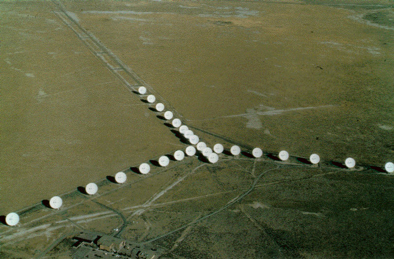 Image of a large antenna array. Several white antennas reside in a green field.
