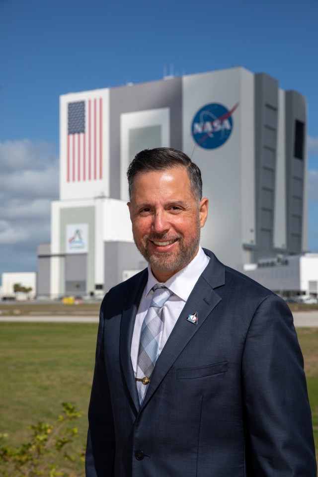 A portrait of Kennedy Space Center's Carlos Monge with the Vehicle Assembly Building in the background.