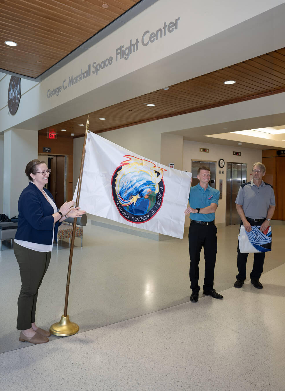 Marshalls commercial crew support team members display the Crew-7 flag in the lobby of Building 4221 on Aug. 23 during a ceremony ahead of the Crew-7 launch.