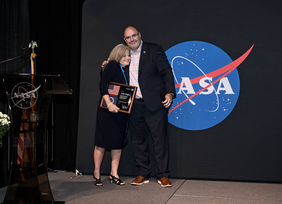 Former Center Director Jody Singer, left, hugs Acting Center Director Joseph Pelfrey after being presented with a plaque honoring her 38 years with NASA and Marshall.