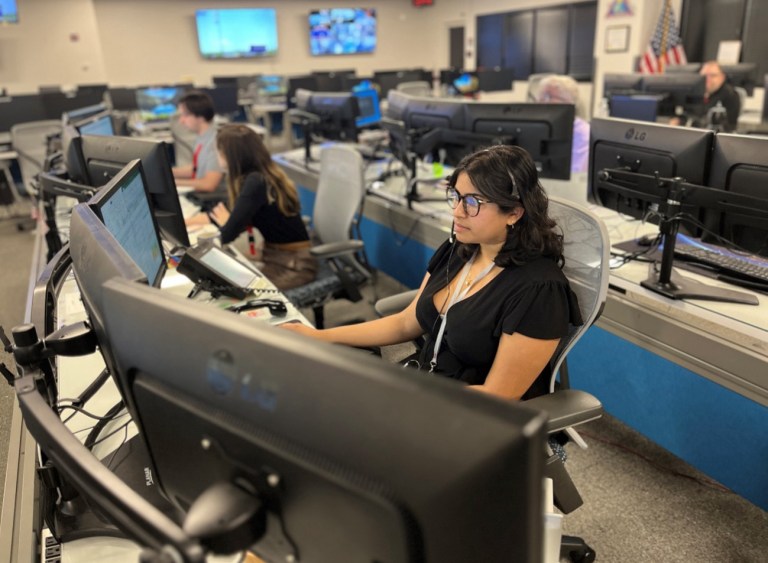 Photo of three people working at a long desk.