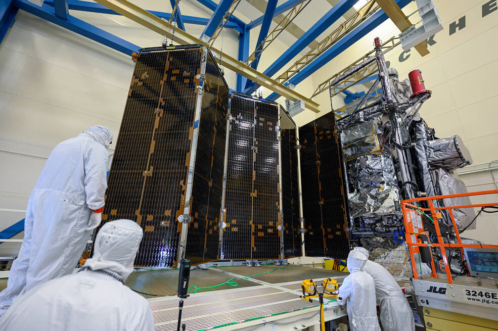 Technicians in clean suits stand around the GOES-U, which is a multiple solar panels partially extended out.