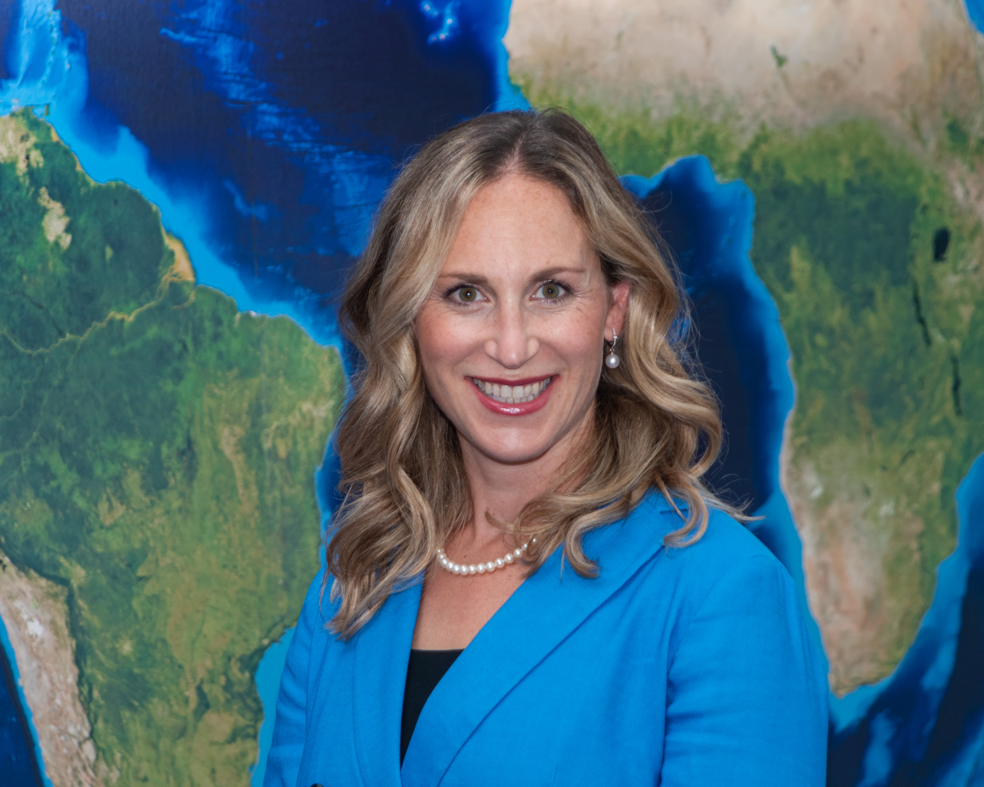 portrait of woman in blue blazer standing in front of an image of Earth