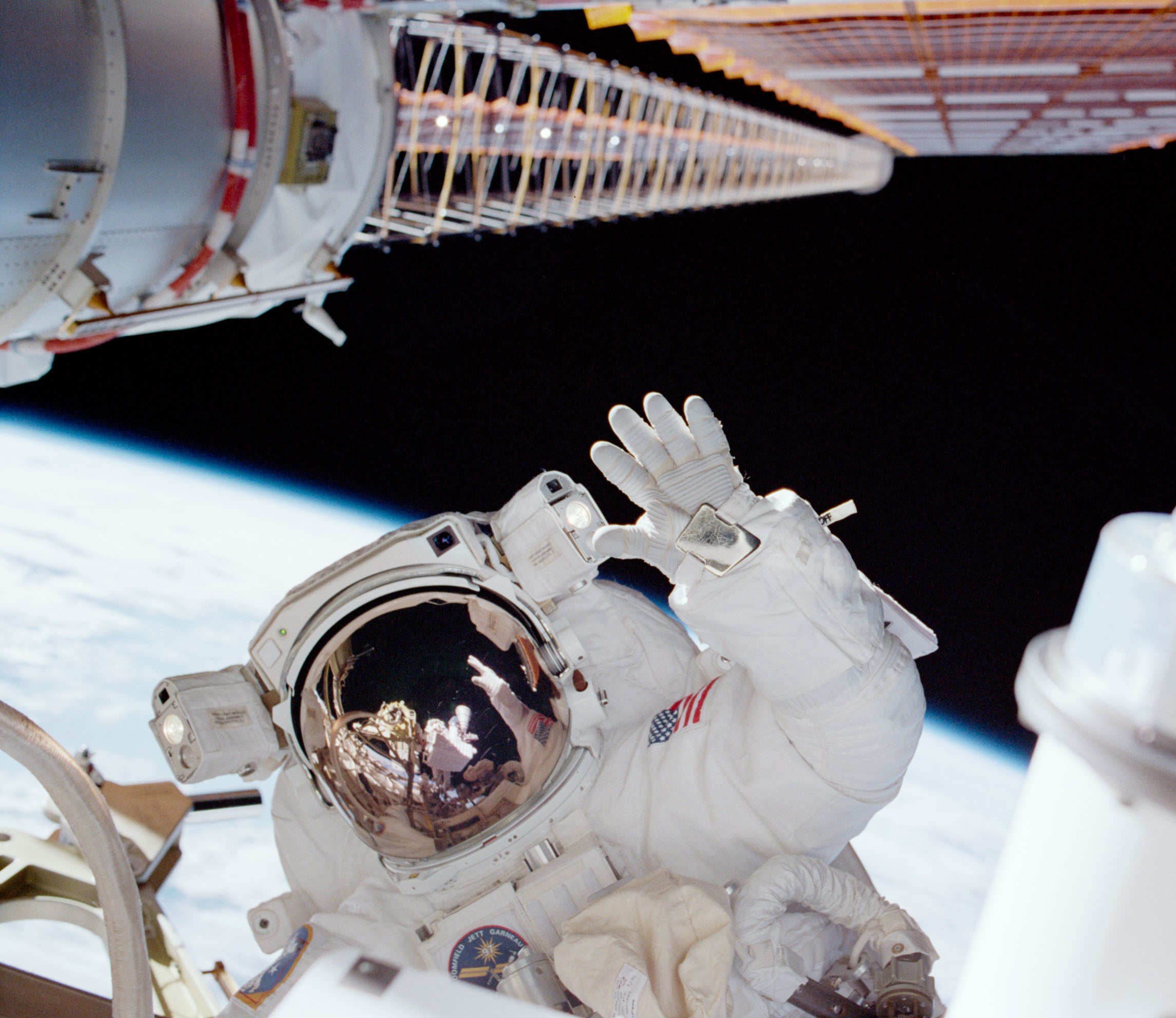NASA astronaut Carlos I. Noriega waves to the camera as he installs the P6 truss and solar arrays.