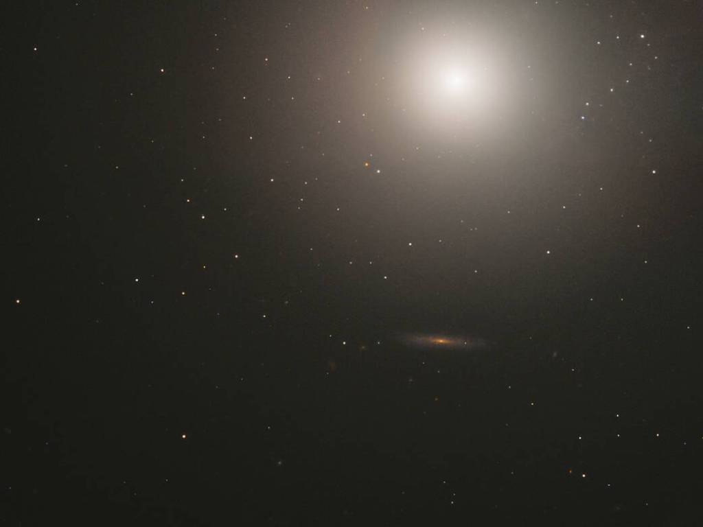 Upper-right quadrant is filled by a sphere of stars with a bright core near the top. Outward from the core, the sphere is more diffuse. A reddish-orange, edge-on galaxy is in the lower-right quadrant of the image.