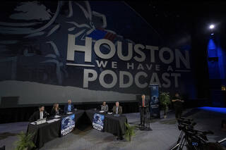 (From left) your host, Gary Jordan, Angela Hart, Steve Koerner, Dina Contella, and Steve Stich are gathered at tables as President and CEO of Space Center Houston, William Harris, stands at a podium to introduce the live recording. 