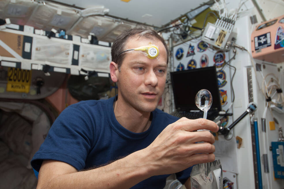 NASA astronaut Tom Marshburn wears a Drager Double Sensor on his forehead while manipulating a water bubble as it floats in microgravity.