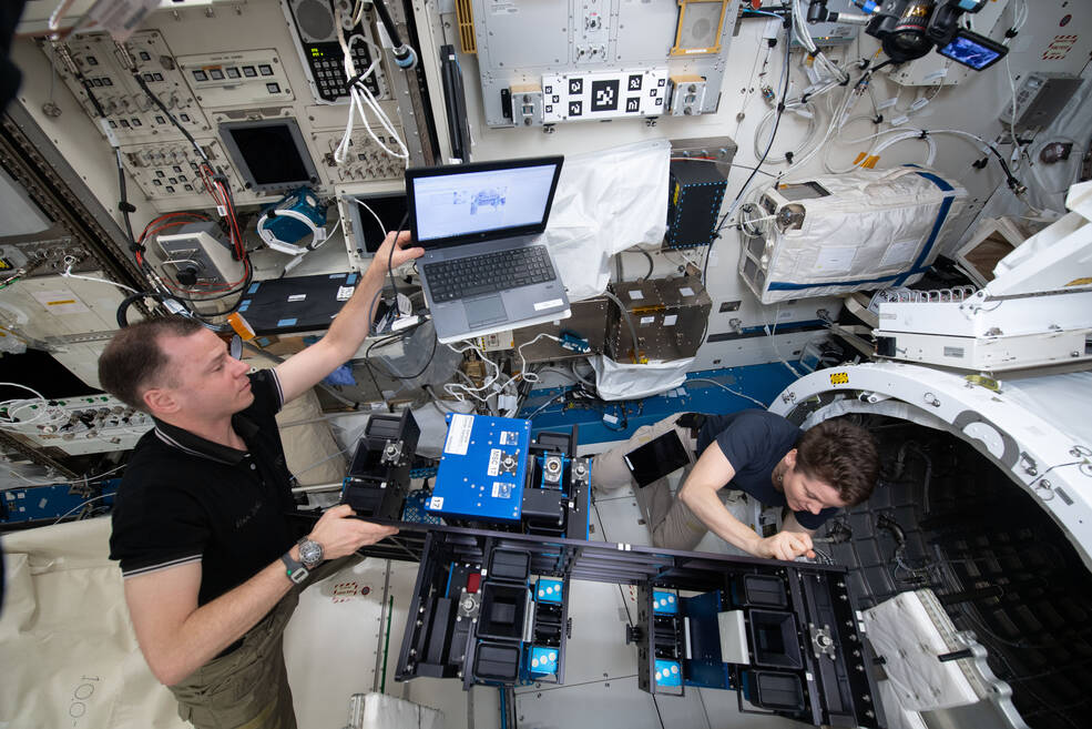 Two astronauts are shown installing sample cartridges on the MISSE-FF inside the JEM prior to deploying the system to the exterior of the station.