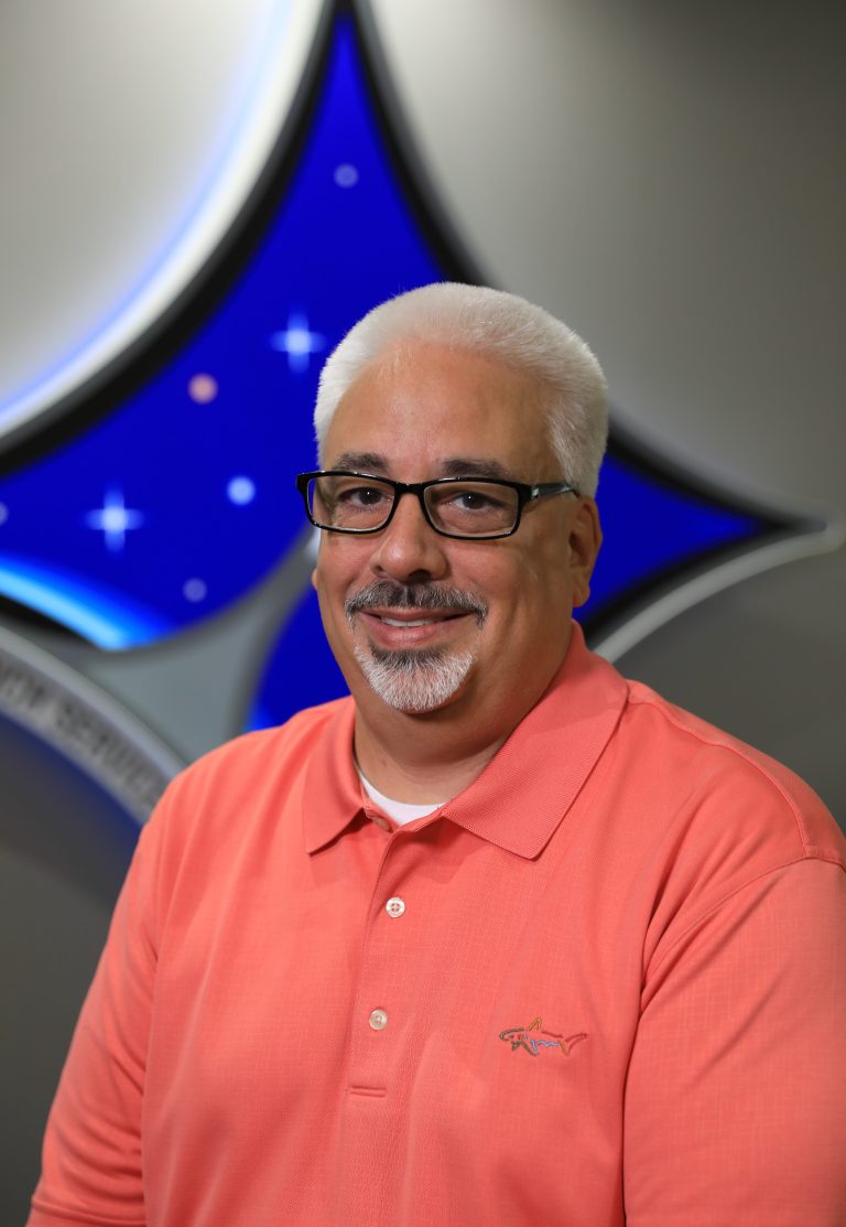 A portrait of Kennedy Space Center's Jorge Piquero with the Launch Services Program insignia in the background.