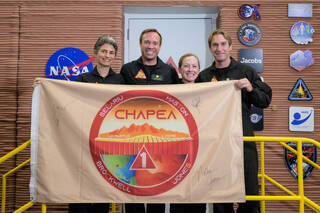The CHAPEA Mission 1 crew poses for a photo with their mission flag which includes the CHAPEA patch. From left are Anca Selariu, science officer; Nathan Jones, medical officer; Kelly Haston, commander; and Ross Brockwell, flight engineer. 