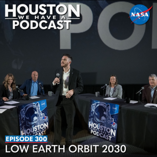 A wide shot of a stage. In the center is the host, Gary Jordan. Behind (from left) is Angela Hart, Steve Koerner, Dina Contella, and Steve Stich all sitting at tables as they discuss the future of a presence in low Earth orbit. 
