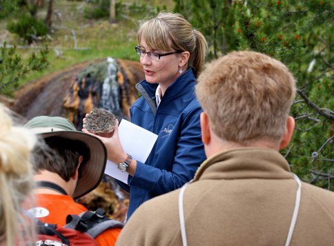 Niki Parenteau in glasses and a dark blue jacket holding a rock while teaching teachers