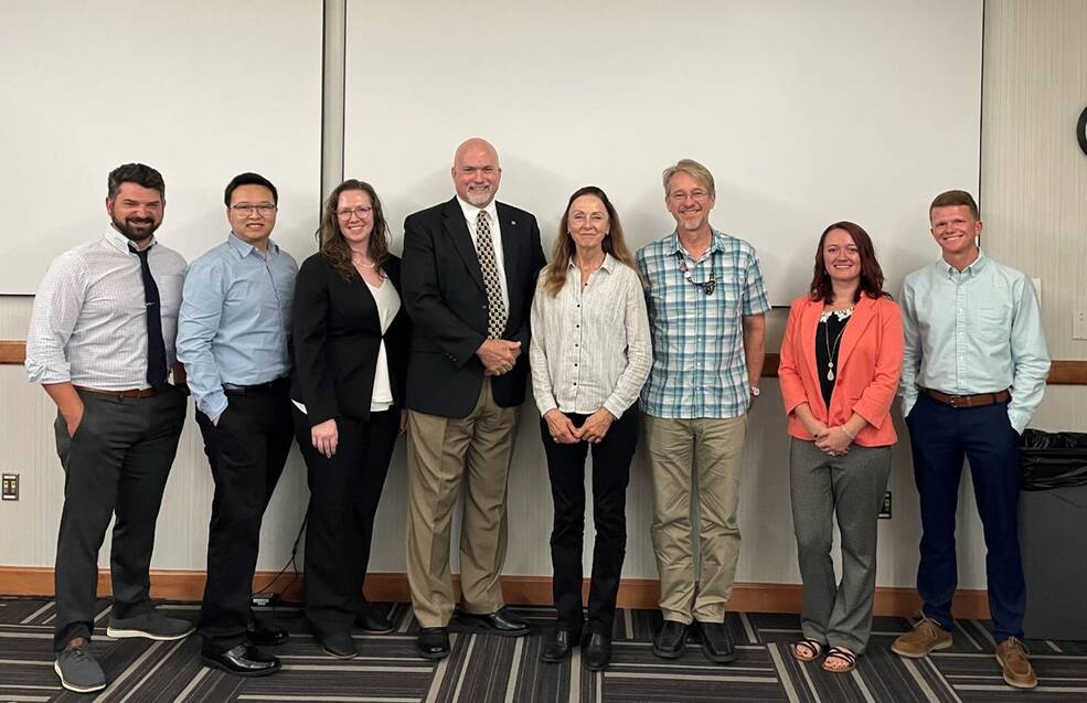 A group of people stand in front of a wall smiling in their work attire.