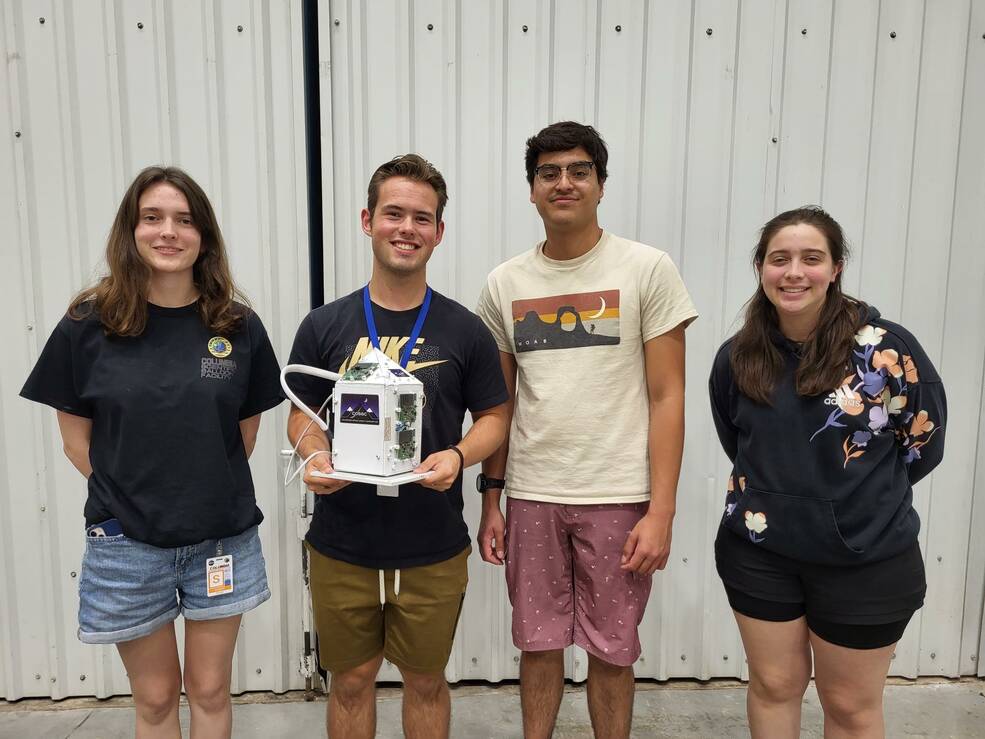 Four university students pose with a small model of the High-Altitude Student Platform payload.