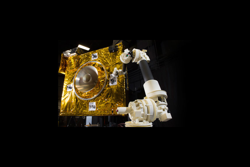 A prototype model of the robotic servicing arm stands in front of a satellite mockup