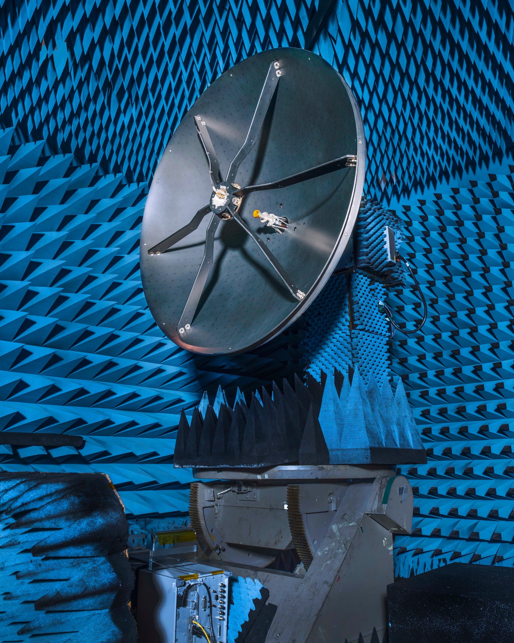Roman’s high-gain antenna - a large, gray dish, about the height of a refrigerator, in a test chamber that is covered in blue spiked-shaped foam. A small circle is elevated in the middle of the antenna disk by six metal strips.