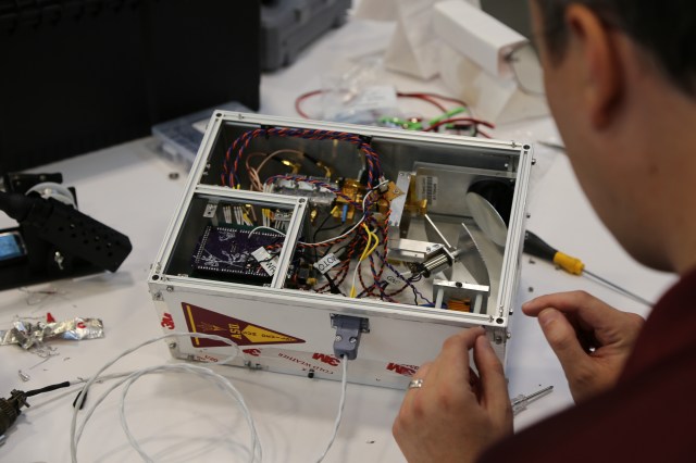 Researcher works on technology in box with top removed, revealing wires and other components.