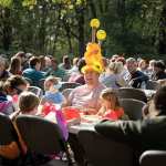 A man with an open-mouthed smile wears a balloon hat made at the Fall Family Fest alongside children who are also enjoying their balloon toys during a Bingo round.