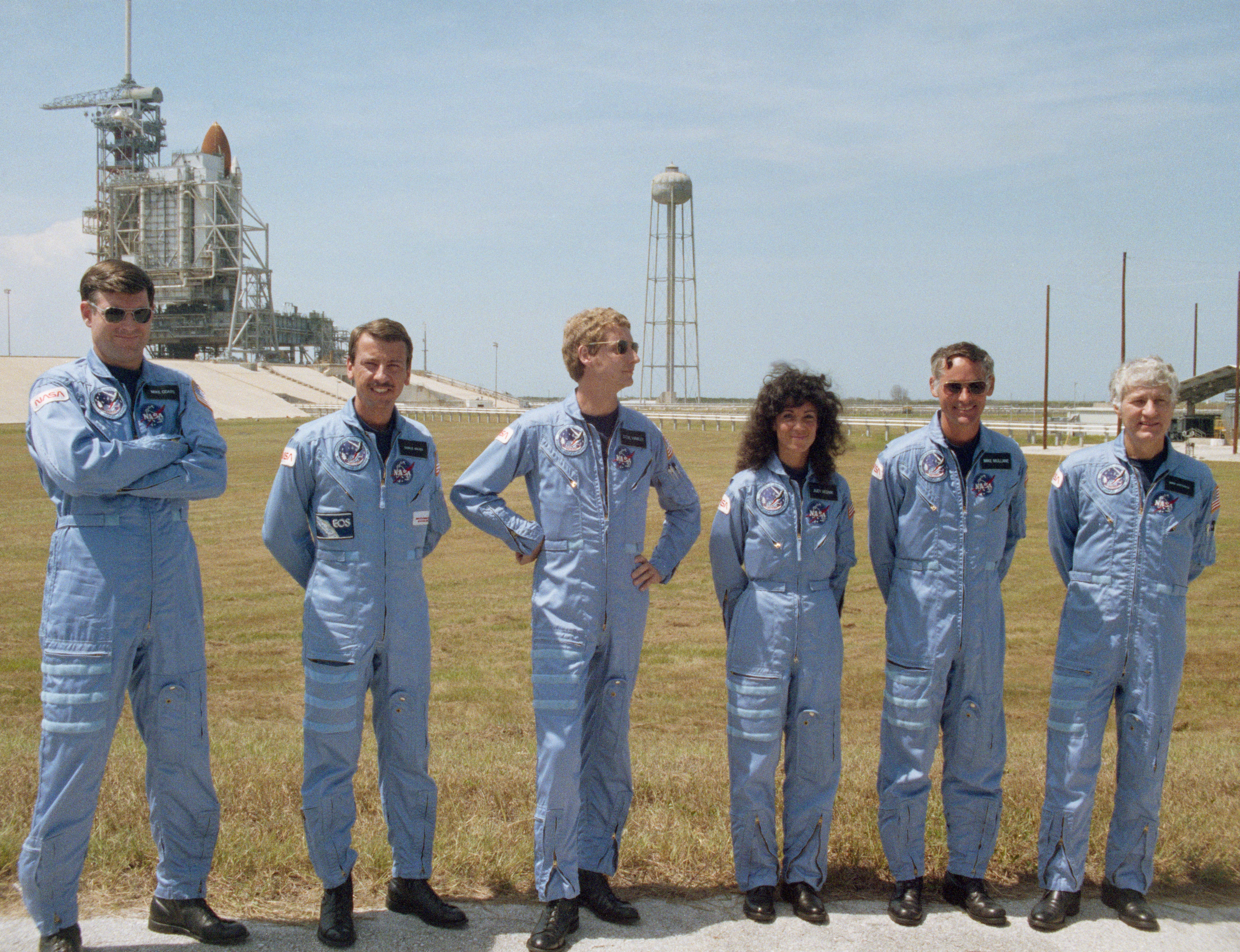 With Discovery as a back drop, STS-41D astronauts Michael L. Coats, left, Charles D. Walker, Steven A. Hawley, Judith A. Resnik, Richard M. “Mike” Mullane, and Henry W. “Hank” Hartsfield pose for photographers following the countdown demonstration test