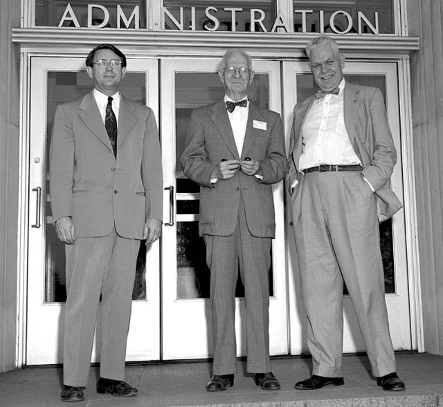 Three men in front of building entrance.