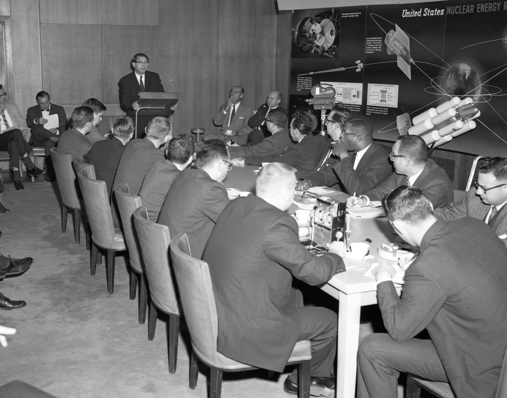 Man addressing seated reporters.