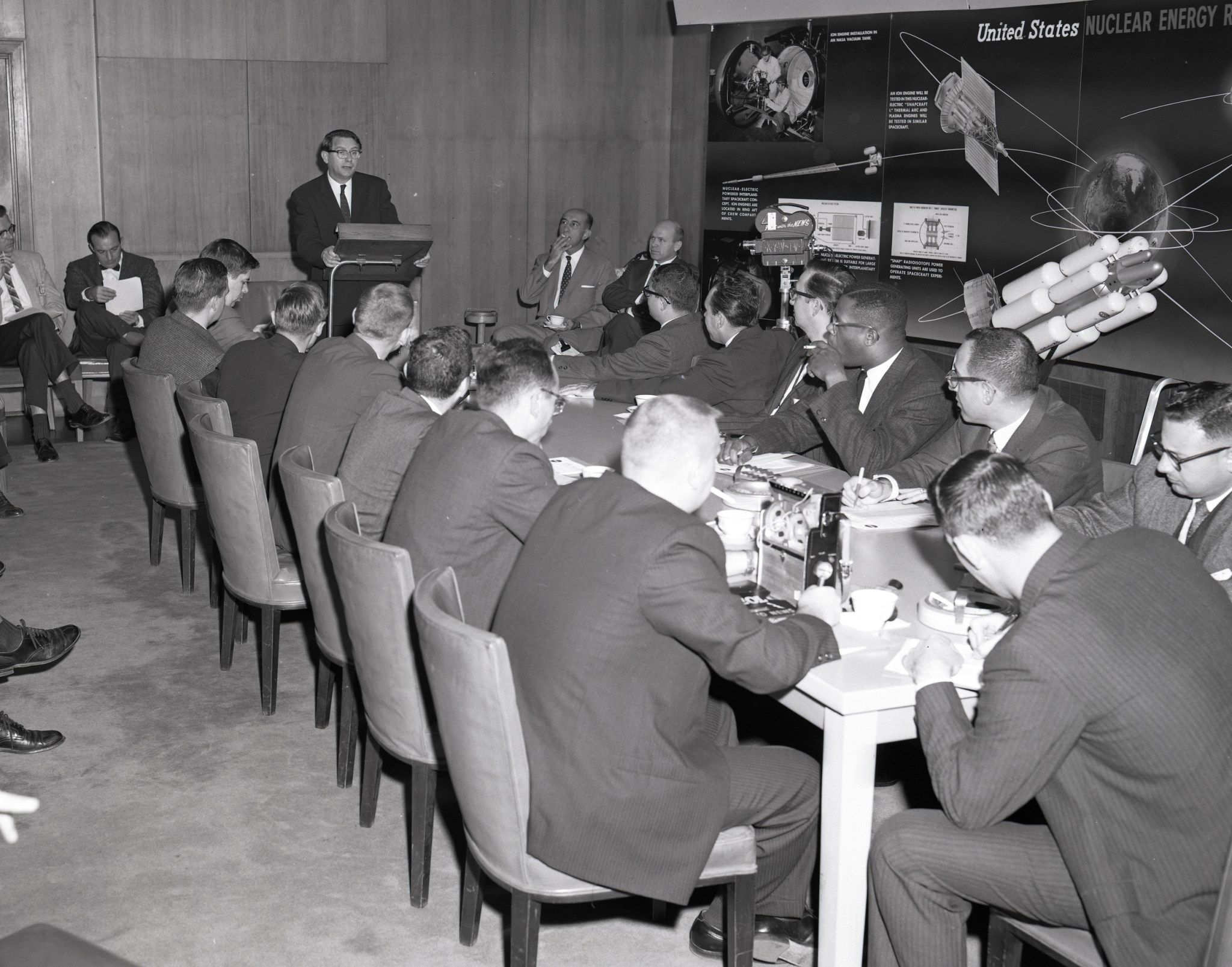 Man addressing seated reporters.