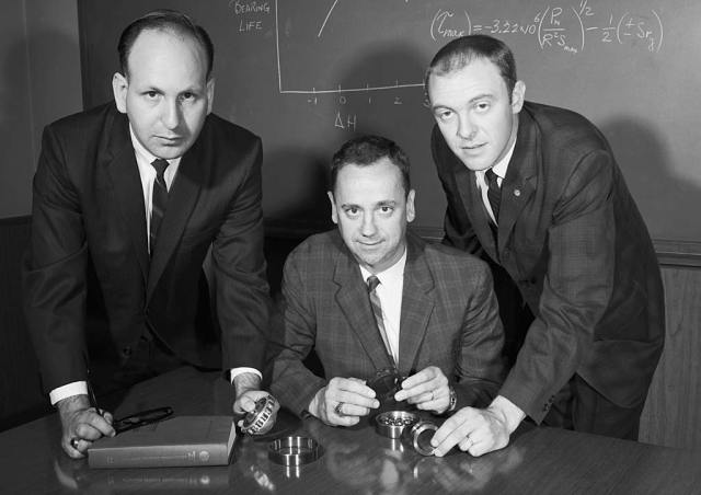 Three men in front of blackboard.