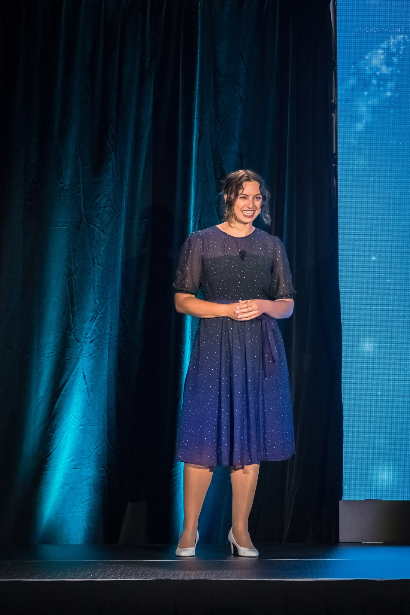 Darcy DeAngelis smiles as she addresses an audience from a stage.