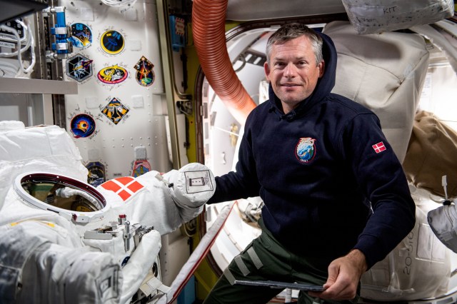ESA (European Space Agency) astronaut and Expedition 70 Commander Andreas Mogensen works on a spacesuit with his nation's flag patch (Mogensen is from Denmark) inside the Quest airlock aboard the International Space Station.