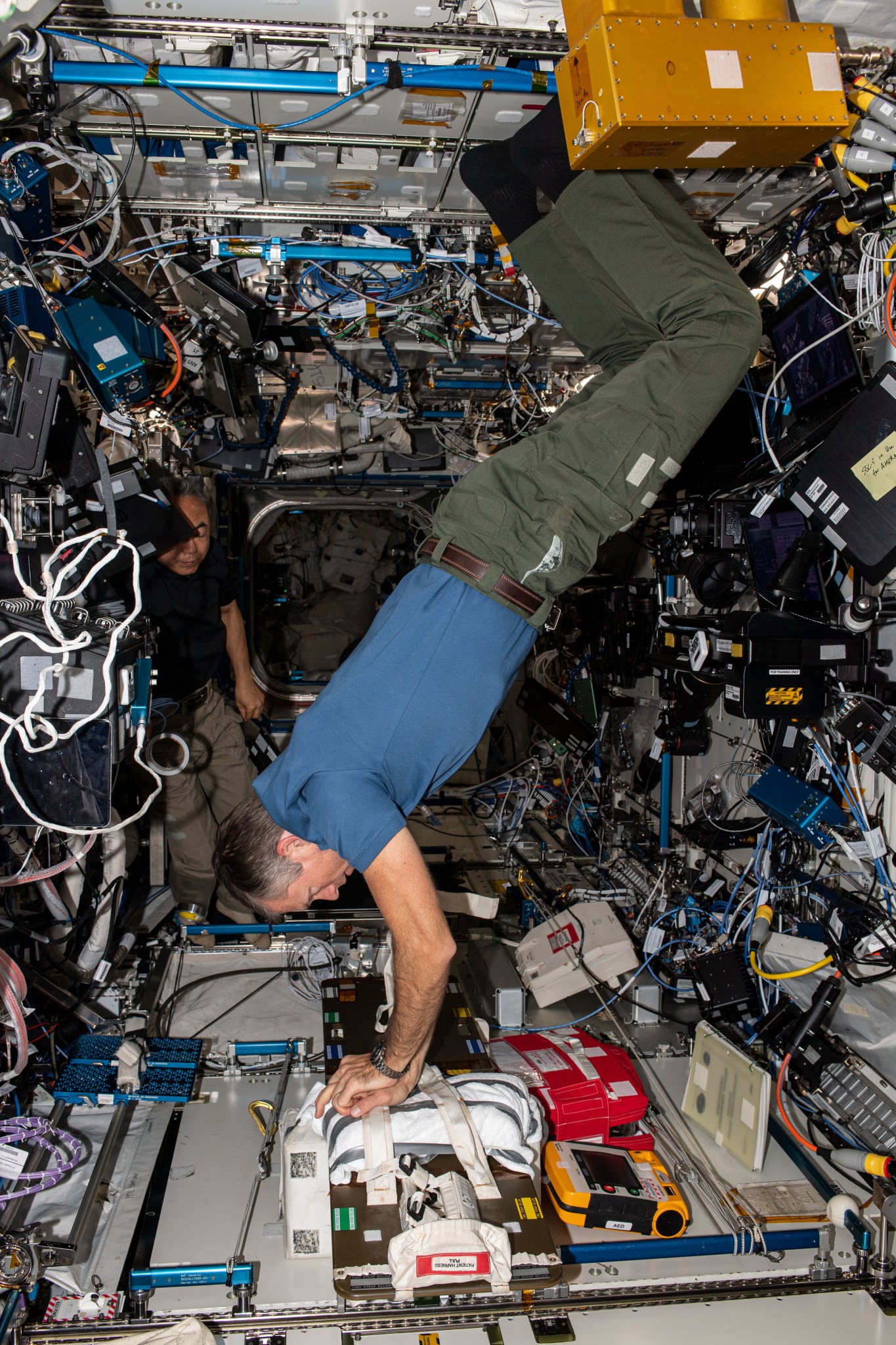 Expedition 70 Commander Andreas Mogensen of ESA (European Space Agency) stabilizes himself in the microgravity environment and practices chest compressions, or cardiopulmonary resuscitation (CPR), inside the International Space Station's Destiny laboratory module. In back, Flight Engineer Satoshi Furukawa of JAXA (Japan Aerospace Exploration Agency) observes the regularly scheduled emergency training session.