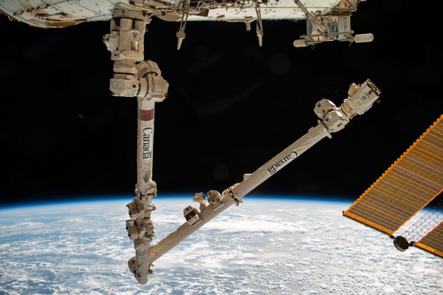 The Canadarm2 robotic arm is pictured extending from the International Space Station while orbiting 260 miles above the Pacific Ocean near the Aleutian Islands.