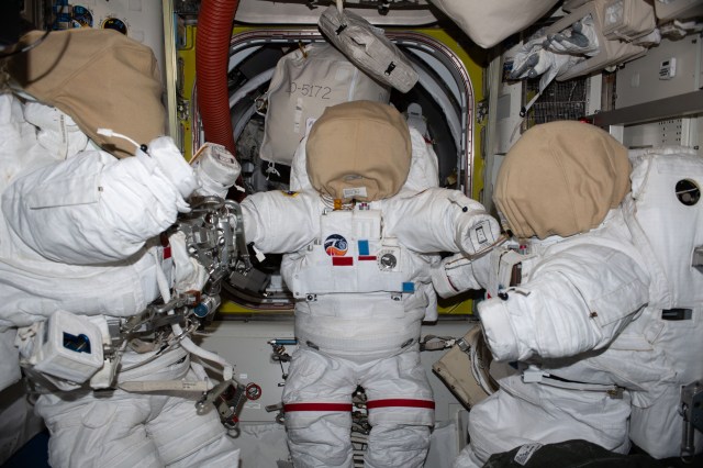 Three spacesuits are pictured after being prepared inside the International Space Station's Quest airlock ahead of upcoming spacewalks.