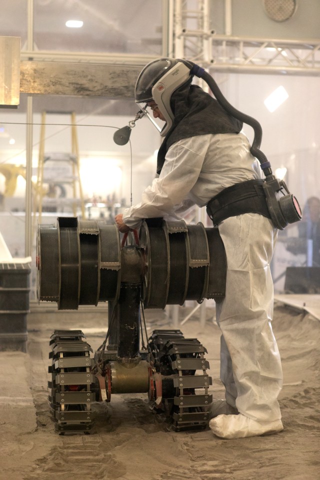 A robotics engineer makes adjustments to the Regolith Advanced Surface Systems Operations Robot (RASSOR) during testing in the regolith bin inside Swamp Works at NASA’s Kennedy Space Center.