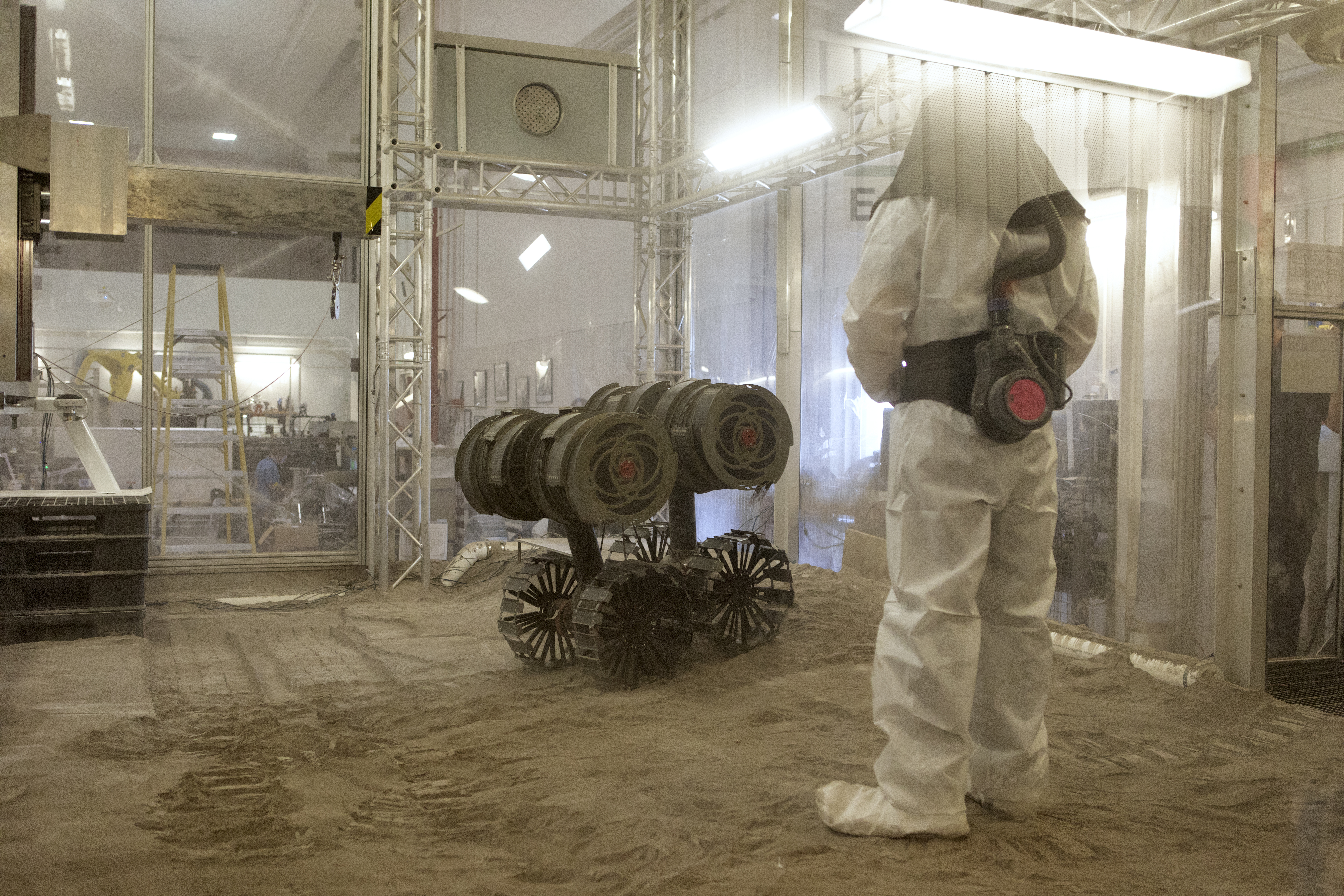 A robotics engineer makes adjustments to the Regolith Advanced Surface Systems Operations Robot (RASSOR) during testing in the regolith bin inside ...