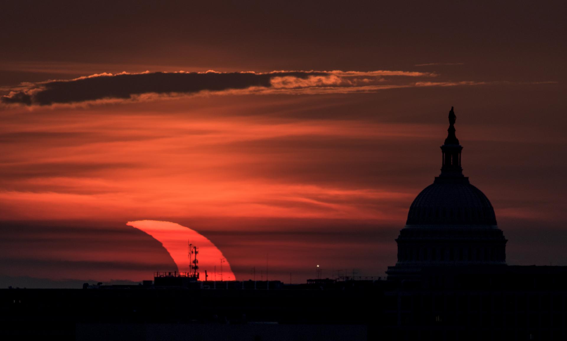 Un'eclissi solare parziale è vista mentre il sole sorge a sinistra del Campidoglio degli Stati Uniti, giovedì 10 giugno 2021, visto da Arlington, Virginia.  L’eclissi solare anulare o “anello di fuoco” è visibile solo ad alcune persone in Groenlandia, Russia settentrionale e Canada.