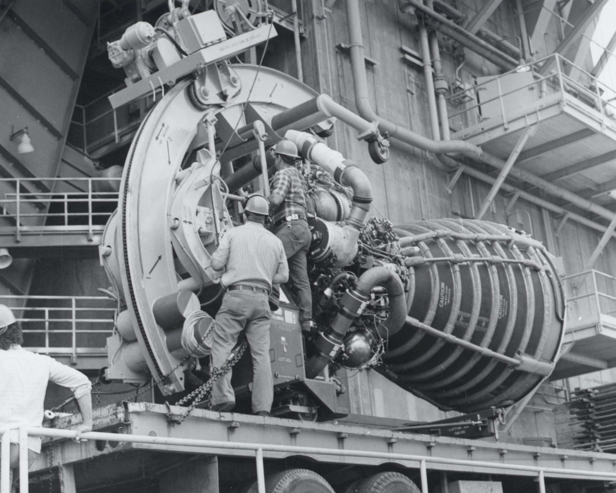 a black and white image of work crews preparing to lift a space shuttle main engine for testing at Stennis Space Center in 1979