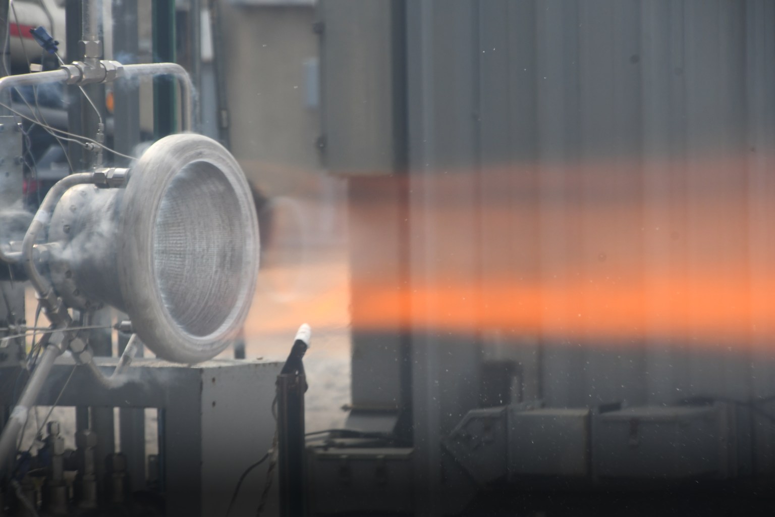 A hot fire test of a 3D printed nozzle is shown with an orange fire being expelled at Marshall Space Flight Center in Huntsville, Alabama.