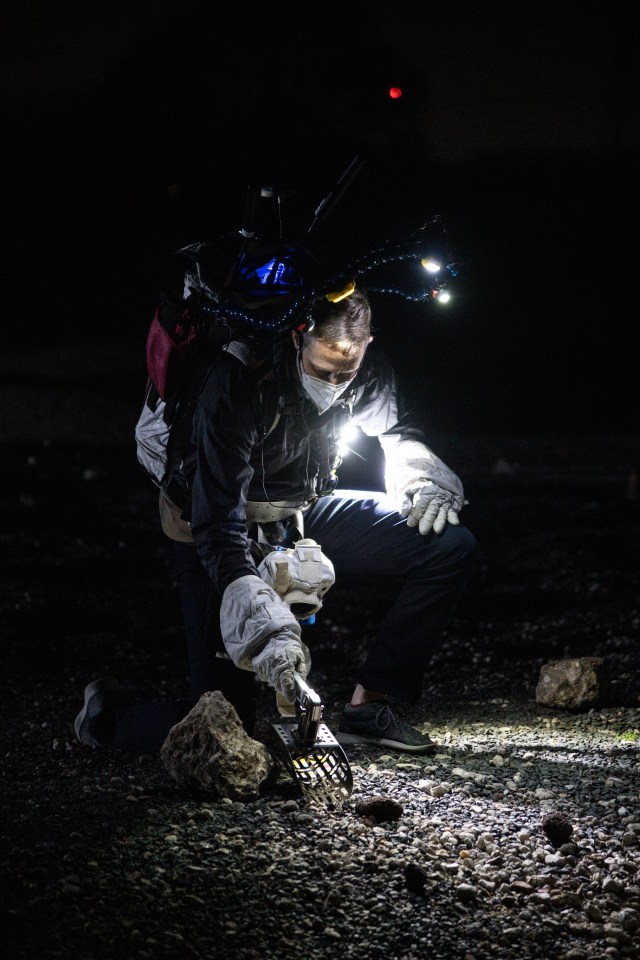 An engineer practices picking up geology samples using a rake during a night time simulated moonwalk at NASA's Johnson Space Center.